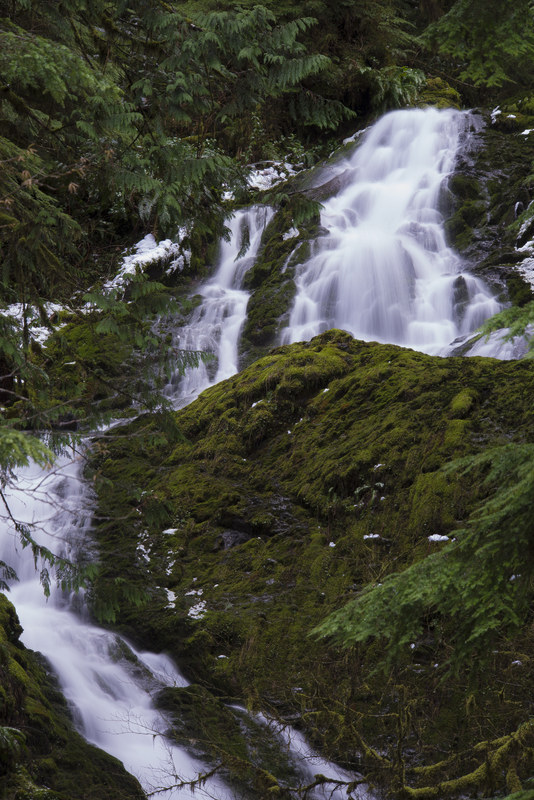 Long exposure waterfall cascading over snow-dusted moss-covered rocks in a winter forest