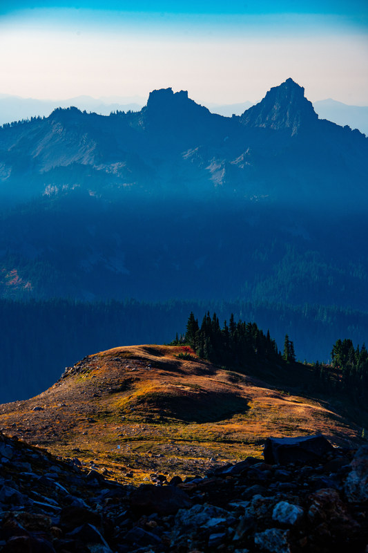 Lone alpine butte lit by warm light against deep blue layered Cascade mountain ridgelines