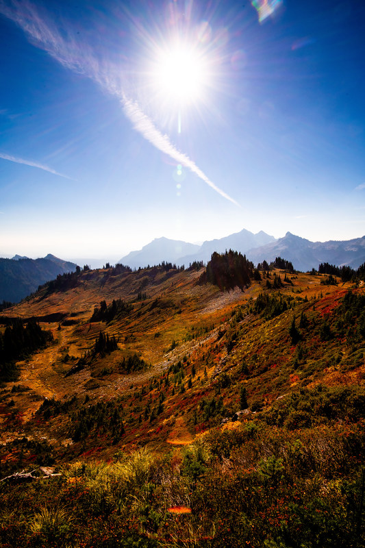 Autumn alpine meadow with warm sunburst, red and orange foliage, and distant mountain peaks